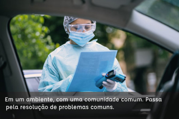 Uma jovem, usa touca, mascara e jaleco descartáveis, está com óculos de proteção de acrílico transparente. Segura uma pasta e um aferidor de temperatura na mão esquerda.  E a legenda: “em um ambiente, com uma comunidade comum. Passa pela resolução de problemas comuns.